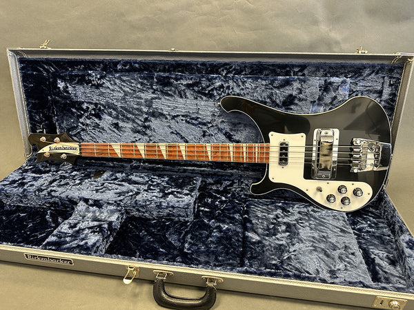Rickenbacker black electric bass guitar with white pickguard and triangular inlays in open gray hardshell case with dark blue interior lining