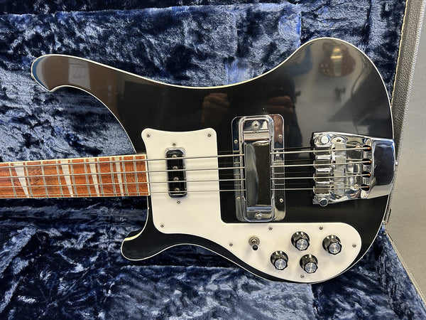 Black electric bass guitar with white pickguard and chrome bridge hardware resting in blue plush-lined guitar case