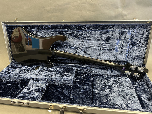 Back view of black Rickenbacker electric guitar inside blue plush-lined hard case with gold latches.
