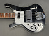 Black and white electric bass guitar with chrome bridge and pickups, four control knobs, and wooden fretboard on gray background