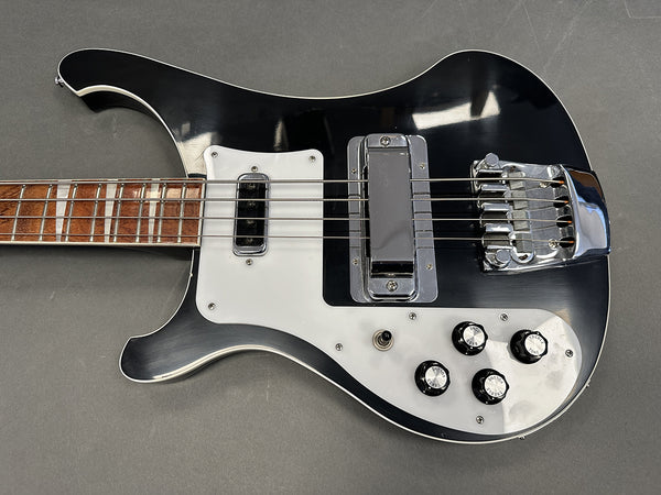 Black and white electric bass guitar with chrome bridge and pickups, four control knobs, and wooden fretboard on gray background