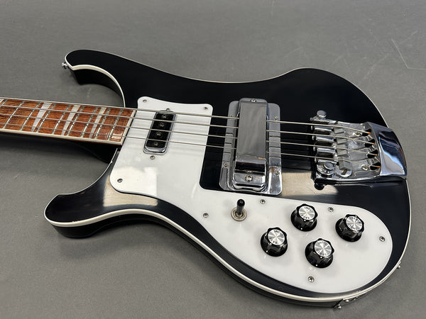 Black electric bass guitar with white pickguard, chrome bridge and pickup, four control knobs, and rosewood fretboard on gray background.