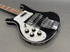 Black electric bass guitar with white pickguard and chrome hardware close-up on gray background