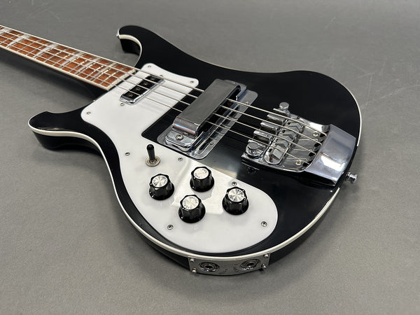 Black electric bass guitar with white pickguard and chrome hardware close-up on gray background
