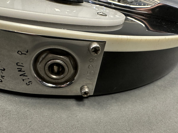 Close-up of guitar output jack plate with serial number 14528 and partial text STAMP R on black electric guitar body edge