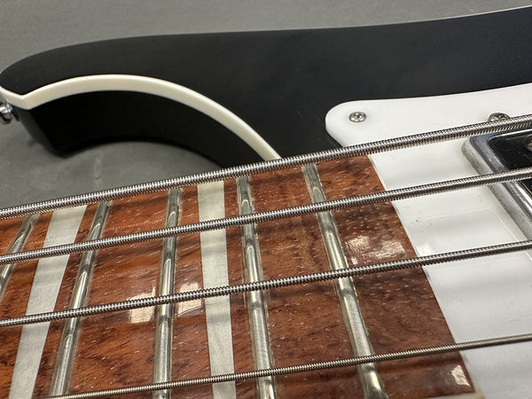 Close-up detail of electric bass guitar fretboard with metal frets, pearl inlays, and black body with white pickguard.