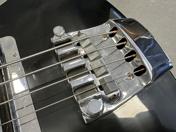 Close-up of black electric bass guitar bridge and strings showing chrome hardware and saddles