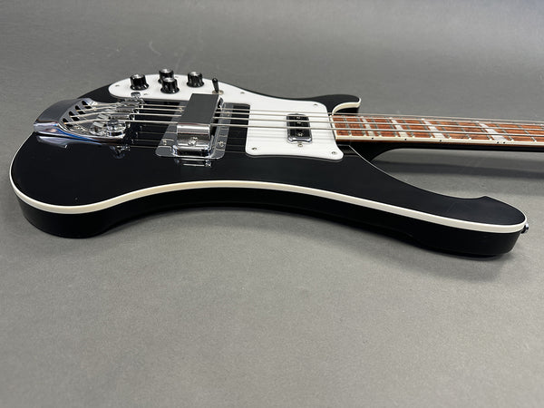 Black electric bass guitar with white pickguard and chrome hardware on gray background