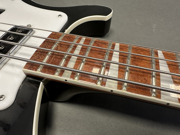 Close-up of black electric bass guitar fingerboard with mother of pearl inlays and silver strings on gray background