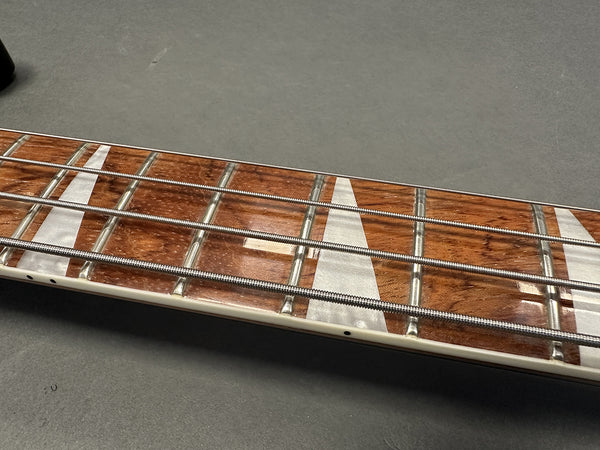 Close-up of electric bass guitar fretboard with pearl inlays and silver frets on dark background
