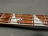 Close-up of electric bass guitar rosewood fretboard with white triangular inlays and metal strings on gray background