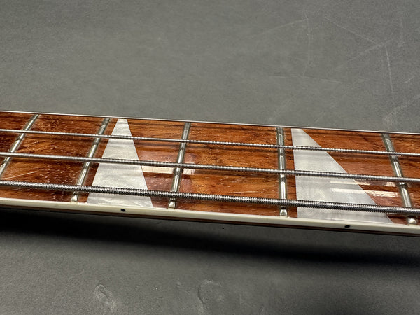 Close-up of electric bass guitar rosewood fretboard with white triangular inlays and metal strings on gray background