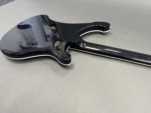 Glossy black electric guitar back with white binding detail on body and neck edge resting on a gray surface