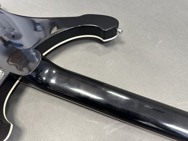 Close-up of glossy black guitar neck and cutaway body with white binding on gray surface