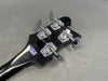 Close-up of black bass guitar headstock with four chrome tuning pegs and Made in America sticker on gray background