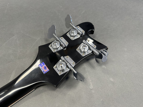 Close-up of black bass guitar headstock with four chrome tuning pegs and Made in America sticker on gray background