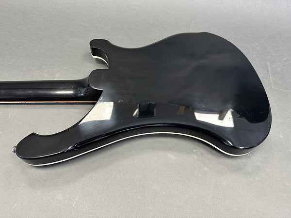 Back view of black electric guitar body with white binding on gray surface