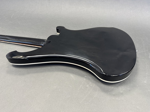 Back side of black electric guitar body with cream binding on a gray background