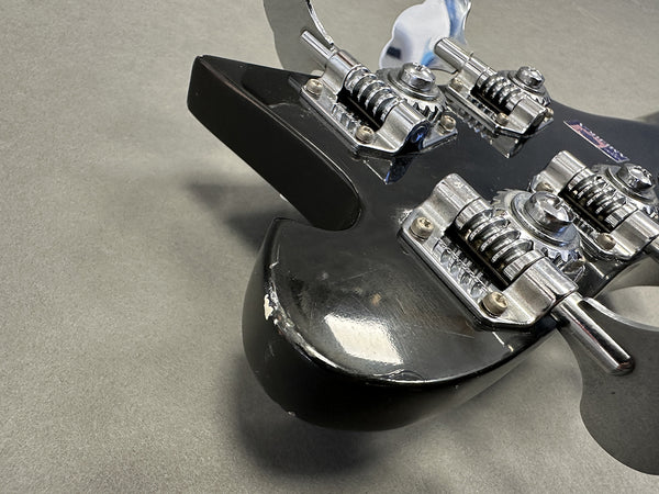 Close-up of black electric guitar body with chrome bridge and tailpiece hardware showing wear and scratches on surface