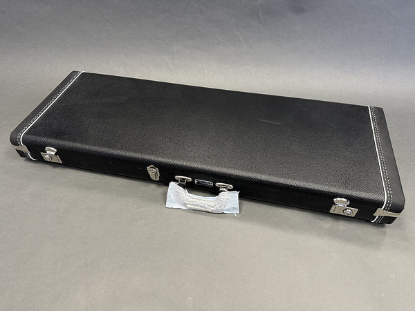 Black hard shell guitar case with silver latches and handle wrapped in protective cloth, closed and placed on gray surface.