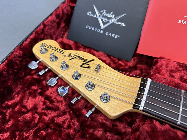 Close-up of Fender Telecaster headstock with chrome tuning pegs on red plush guitar case lining and Fender Custom Care booklet