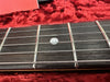 Close-up of guitar fretboard with metal frets and white dot inlay on a red textured surface