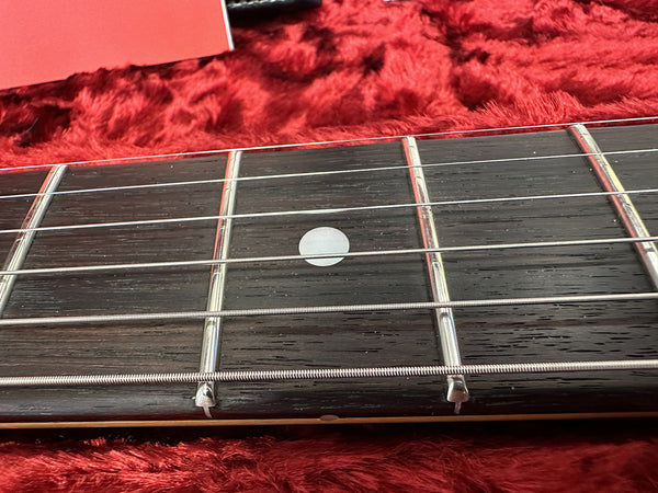 Close-up of guitar fretboard with metal frets and white dot inlay on a red textured surface