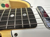 Close-up of electric guitar fretboard with metal frets, mother-of-pearl dot inlays, steel strings, and chrome pickup on white body.