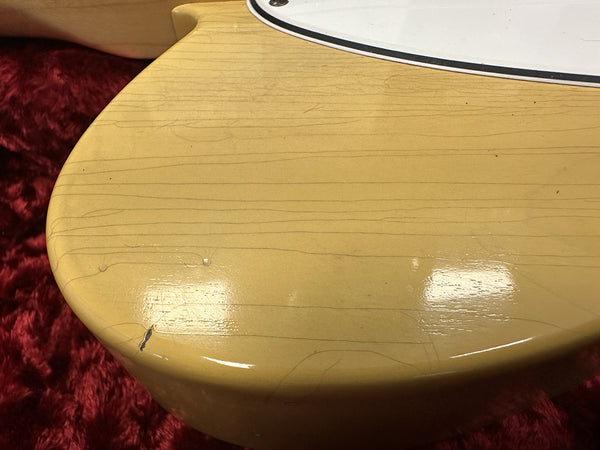 Close-up of worn cream vintage electric guitar body showing finish cracks and chip on red fabric background