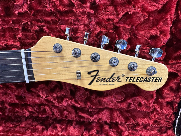 Close-up of Fender Telecaster electric guitar headstock with tuning pegs and natural wood finish on red plush background