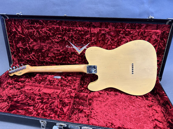 Back view of cream-colored Fender Telecaster electric guitar resting inside open black hard case with red plush interior lining, showcasing neck, tuners, and bolt-on neck plate.