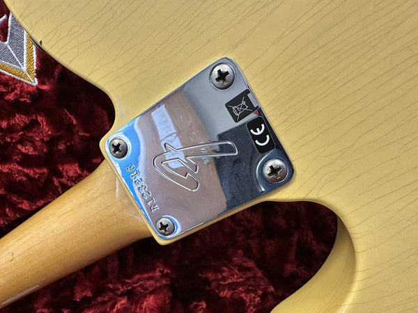 Close-up of Fender electric guitar neck plate with serial number R1233216 on a light wood finish body over red textured background