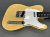 Vintage cream yellow electric guitar body with white pickguard and chrome control plate with two knobs and switch, black fretboard with white dot inlays on gray background