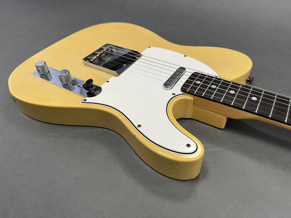 Close-up of vintage yellow electric guitar body with white pickguard and chrome control knobs on gray background