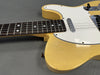 Close-up of vintage yellow electric guitar body and neck with white pickguard and dot inlays on rosewood fretboard on grey background