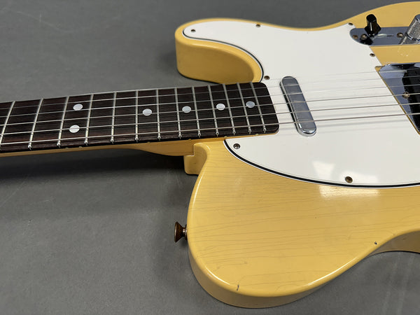 Close-up of vintage yellow electric guitar body and neck with white pickguard and dot inlays on rosewood fretboard on grey background