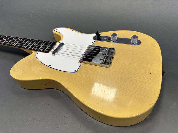Close-up view of vintage yellow electric guitar body with white pickguard and chrome hardware on gray background