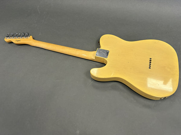 Back view of vintage yellow Fender Telecaster electric guitar showing natural wood neck and chrome neck plate on gray background