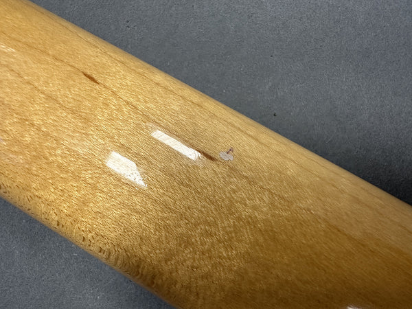 Close-up of guitar neck wood finish with small chip and dent damage on a light brown maple neck against a gray background