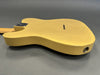 Close-up of vintage yellow electric guitar body with worn finish and visible wood grain on gray background