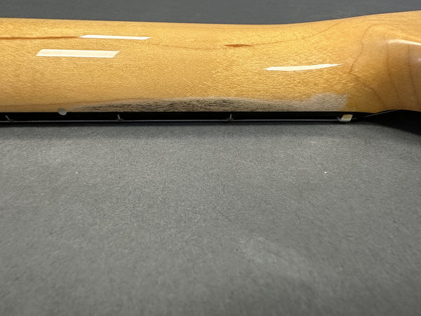 Close-up of light maple guitar neck with black dot position markers and steel string lying on a gray surface, showcasing wood grain and gloss finish