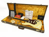 Vintage Fender Custom Shop Stratocaster guitar in white with tortoiseshell pickguard, displayed in open brown hard case with yellow plush interior, accompanied by Fender certificate of authenticity, owner’s manual, guitar strap, and additional documentation.