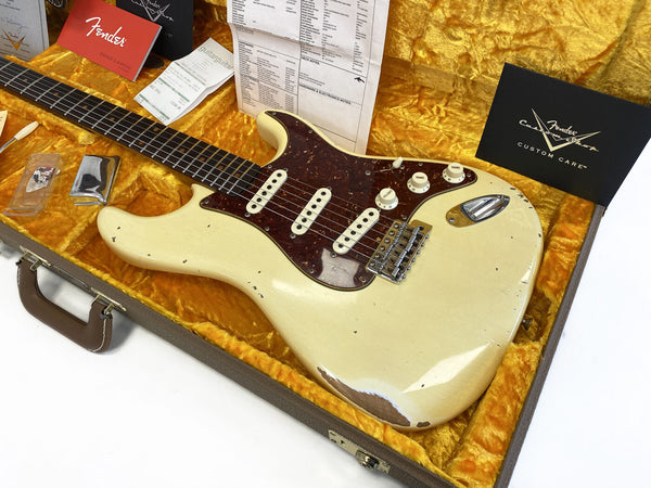 Vintage Fender Stratocaster electric guitar in aged white finish with tortoiseshell pickguard inside a yellow plush-lined hard case with Fender manuals and inspection sheet.