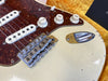 Close-up of vintage electric guitar body with tortoiseshell pickguard, white volume and tone knobs, and chrome bridge and input jack on cream finish with wear marks