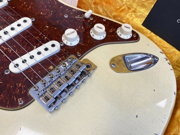 Close-up of vintage electric guitar body with tortoiseshell pickguard, white volume and tone knobs, and chrome bridge and input jack on cream finish with wear marks