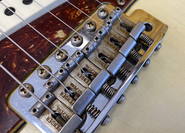 Close-up of vintage Fender guitar bridge and saddle with metal screws and springs on cream-colored body and tortoiseshell pickguard