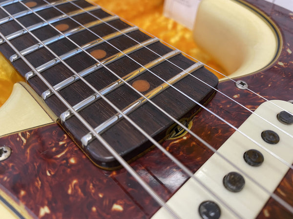 Close-up of electric guitar fretboard with dot inlays, metal frets, strings, and tortoiseshell pickguard detail at Coffee House Guitars