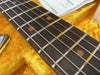 Close-up of vintage electric guitar fretboard with dark wood, metal frets, and strings inside a yellow plush guitar case