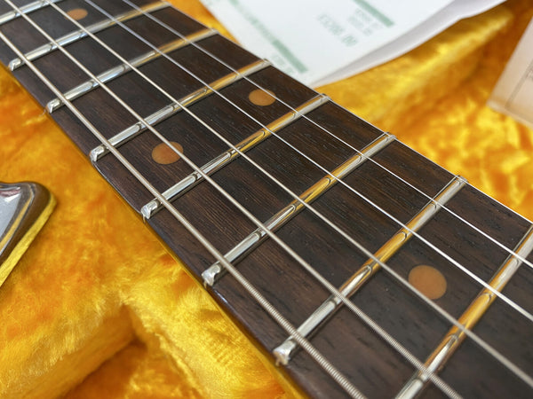 Close-up of vintage electric guitar fretboard with dark wood, metal frets, and strings inside a yellow plush guitar case