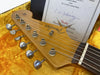 Close-up of Fender Stratocaster guitar headstock with tuning pegs and certificate in yellow plush-lined case